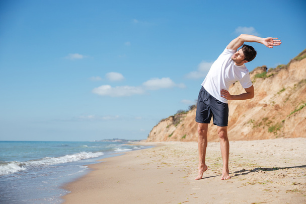 Attraente giovane sportivo in piedi ed esercizio sulla spiaggia
 - Foto, immagini