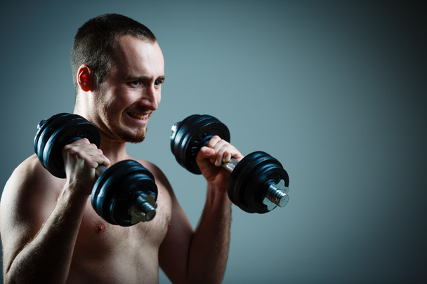 Close up of young man lifting weights over grey background (colo - Photo, Image