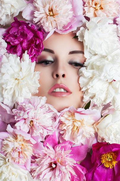 Face of young beautiful woman surrounded by flowers. Peonies closeup. - Foto, afbeelding