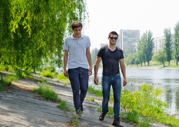 Two young men walking along a riverbank - Foto, afbeelding
