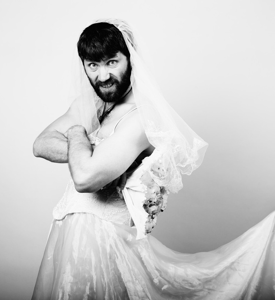 bearded man in a womans wedding dress on her naked body, holding a flower. funny bearded bride, black and white - Photo, image