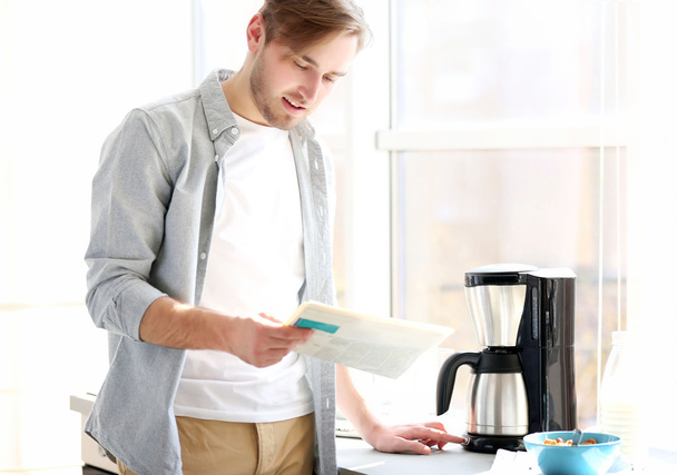 Young man making coffee and reading newspaper in kitchen - Foto, Imagem