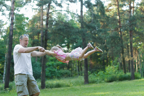 Щасливий батько кружляє навколо своєї дочки в зеленому літньому парку на відкритому повітрі
 - Фото, зображення