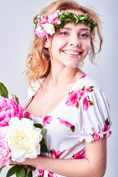 Beauty girl takes beautiful flowers in her hands. Blowing flower. Hairstyle with flowers. Fantasy girl portrait in pastel colors. Summer fairy portrait. Long permed hair. - Fotografie, Obrázek