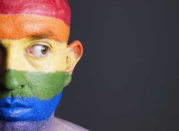 Gay flag painted on the face of a man. Man is looking sideways - Φωτογραφία, εικόνα