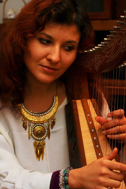 meisje harpiste in witte jurk met juwelen die haar instrument spelen. - Foto, afbeelding