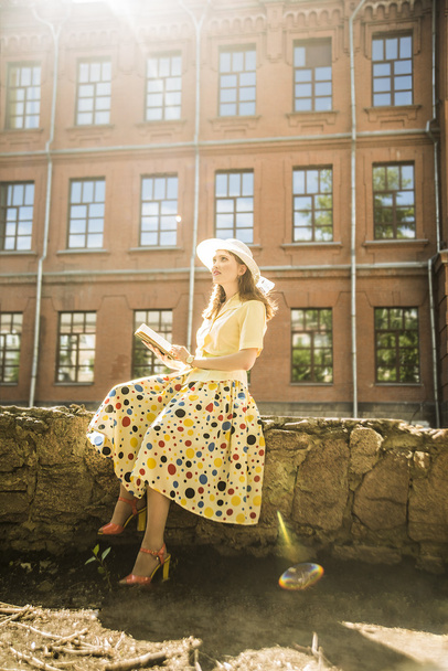 beautiful girl in yellow romantic dress with book near the vintage red brick wall  - Фото, изображение