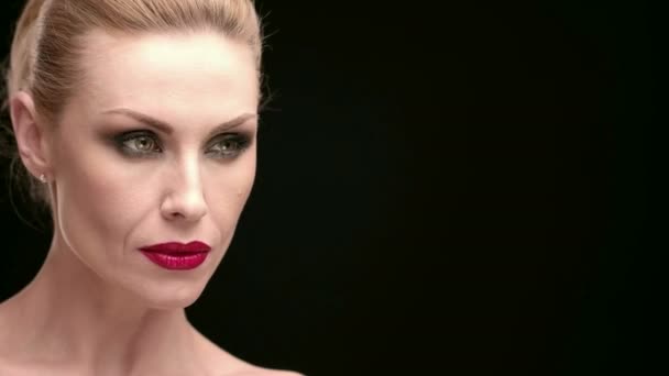 Fierce elegance. Closeup  studio portrait of a mature beautiful blonde woman wearing professional red lips makeup looking at the copyspace on the side on black background - Footage, Video