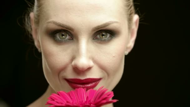 Koket. Çarpıcı bir kırmızı dudaklı kadın mutlu siyah arka plan üzerine kameraya gülümseyen bir çiçek gözleri ile kapalı kokulu closeup kırpılmış - Video, Çekim