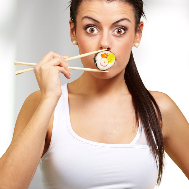 jovem mulher cobrindo a boca com um pedaço de sushi, interior
 - Foto, Imagem