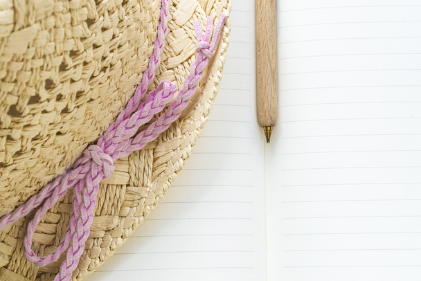 Caderno, caneta e chapéu de palha com um laço rosa
 - Foto, Imagem