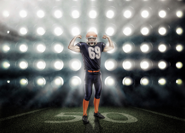 Περήφανοι αμερικανικός παίκτης ποδοσφαίρου σε μπλε ομοιόμορφο φωτίζεται από τους προβολείς - Φωτογραφία, εικόνα