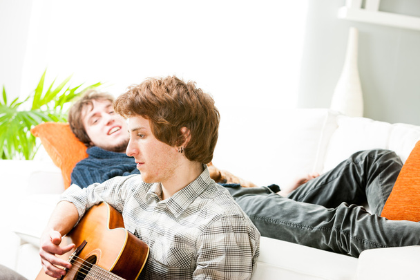 Nuori mies soittaa kitaraa olohuoneen lattialla
 - Valokuva, kuva