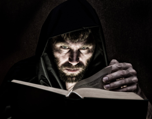 necromancer casts spells from thick ancient book by candlelight on a dark background - 写真・画像