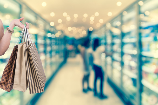 Tenendo borse shoping a mano su sfondo sfocatura supermercato con bokeh, Varie scaffale del prodotto
 - Foto, immagini