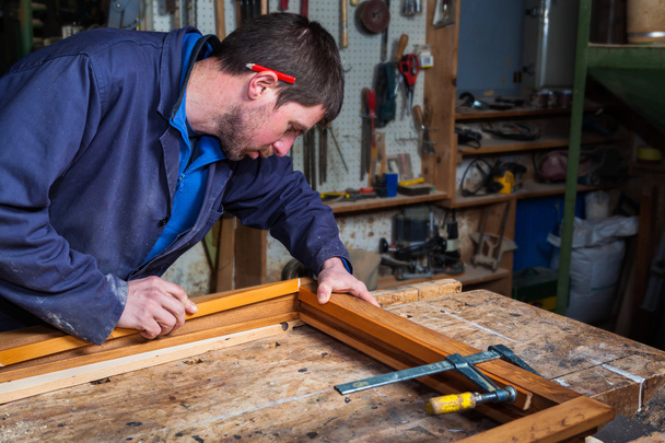 Carpinteiro trabalhando em uma moldura de janela de madeira em sua oficina
 - Foto, Imagem