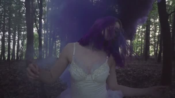 Mooie vrouw in witte jurk en paars haar dansen in forest-Fairytale scène. Video van sensuele schoonheid tussen bomen en paarse rook achter in slow motion. - Video