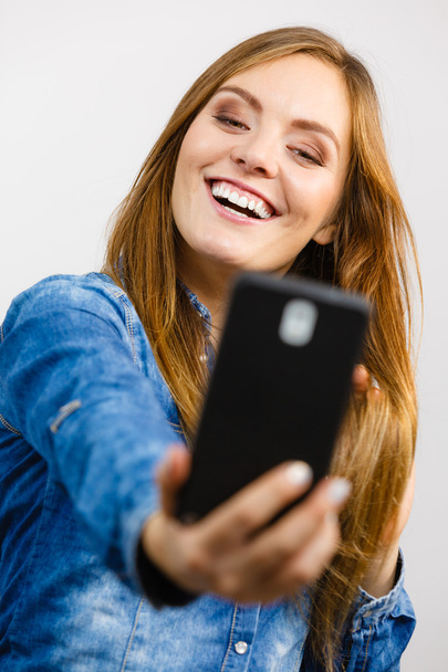 Nainen denim-paidassa ottamassa itsestään kuvaa puhelimella
 - Valokuva, kuva