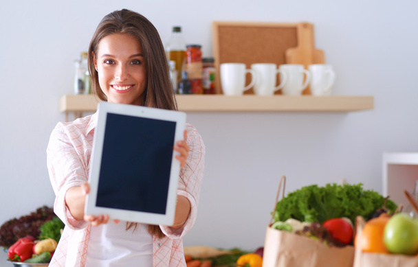 Young woman using a tablet computer to cook in her kitchen . - Foto, Bild