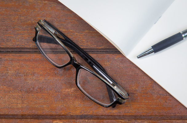 caderno aberto com caneta e óculos em um fundo de madeira
 - Foto, Imagem