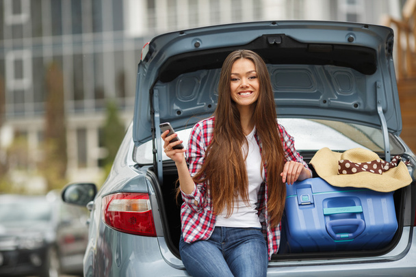 Young woman sitting in the car trunk with suitcases - Foto, afbeelding