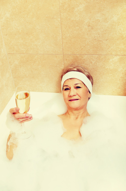 Senior woman relaxing in bath with glass of champagne - Foto, Imagem