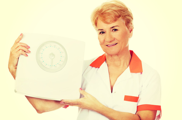 Smile elderly female doctor or nurse holds weigh scale - Photo, Image