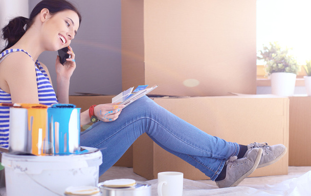 Woman choosing paint colour from swatch for new home sitting on wooden floor - Photo, image