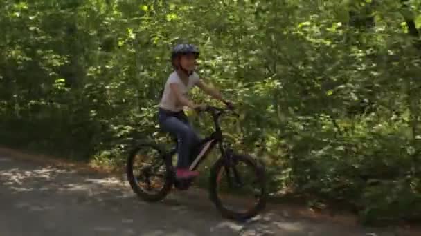little girl rides her bike on a forest trail - Felvétel, videó