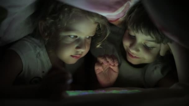 two little girls sisters playing on a tablet PC hiding under a blanket - Séquence, vidéo