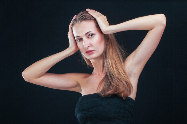 Pretty woman holding head in hands standing against black backgr - Fotografie, Obrázek