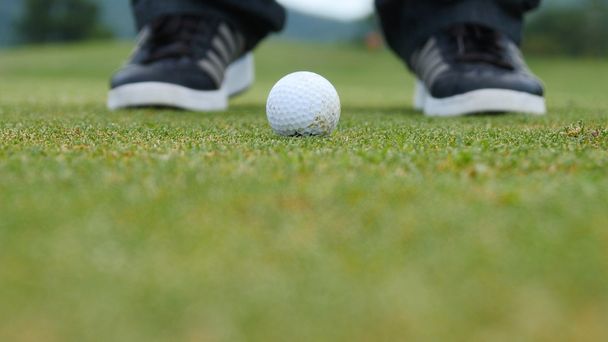 Игрок в гольф бросает мяч в лунку, видны только ноги и железо
 - Фото, изображение