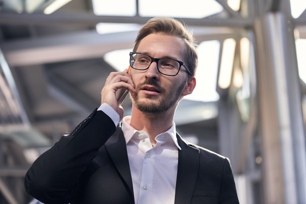 Portrait of handsome businessman in suit and eyeglasses speaking on the phone in airport - Fotó, kép