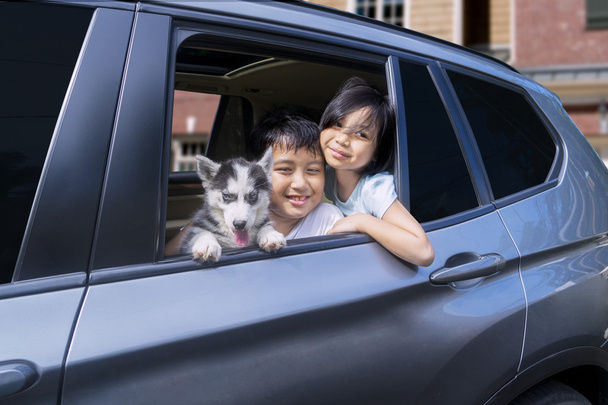 Cheerful children with puppy in the car - Foto, imagen