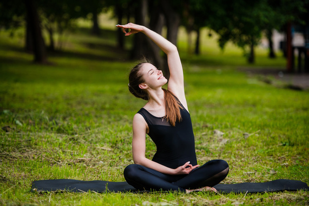 Hermosa joven haciendo ejercicio de estiramiento sobre hierba verde en el parque. Entrenamiento de yoga
 - Foto, imagen