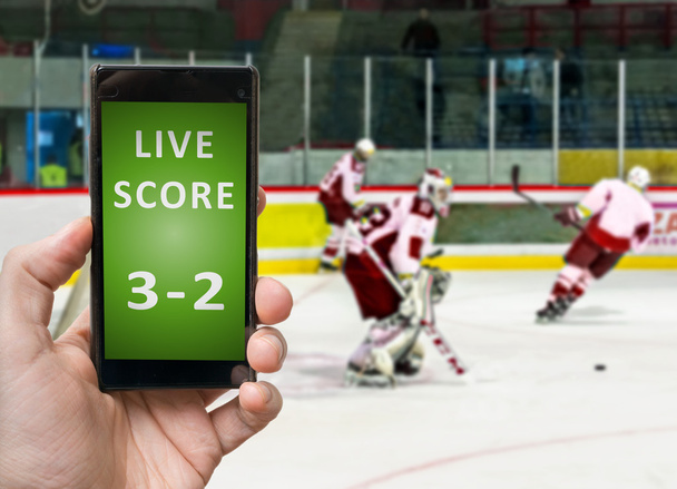 Człowiek jest oglądanie hokeja na lodzie i posiada smartfona w parze z na żywo. - Zdjęcie, obraz