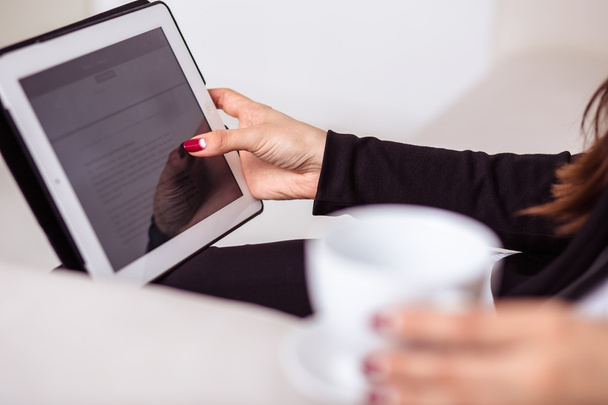 Mulher bebe café e trabalha em um computador tablet na zona lounge do escritório
 - Foto, Imagem
