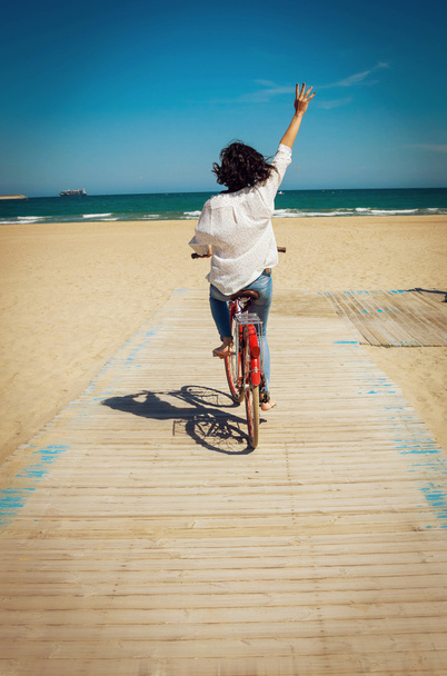 Happy young woman riding a bike on a beach - Fotoğraf, Görsel