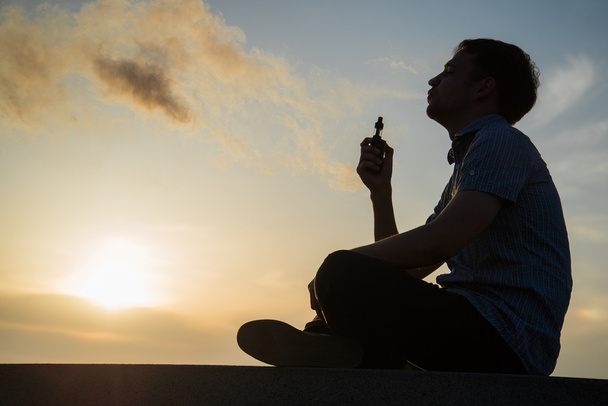 Homme fumant vaping e-cigarette vape mode boîte sur coucher de soleil doré
 - Photo, image