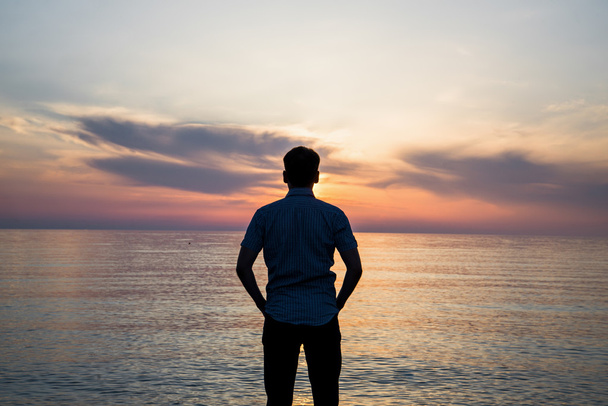 Młody człowiek, stojąc na plaży przed widok na morze na zachód lub wschód słońca i myślenie o jego przyszłość. Widok z tyłu - Zdjęcie, obraz