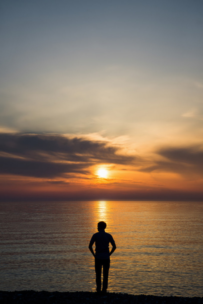 Jeune homme debout à la plage devant une vue imprenable sur la mer au coucher ou au lever du soleil et penser à son avenir. Vue arrière
 - Photo, image