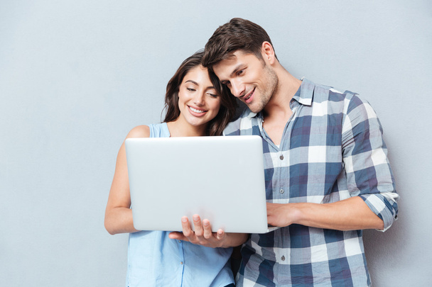 Portrait of happy young couple using laptop over gray background - Foto, imagen