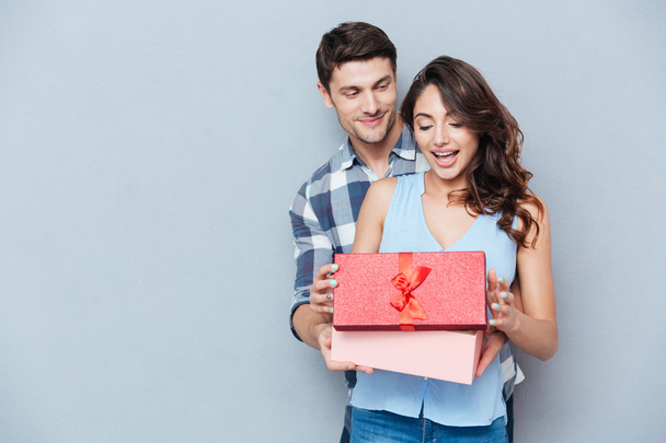 Young woman receiving gift from her boyfriend over gray background - Foto, imagen
