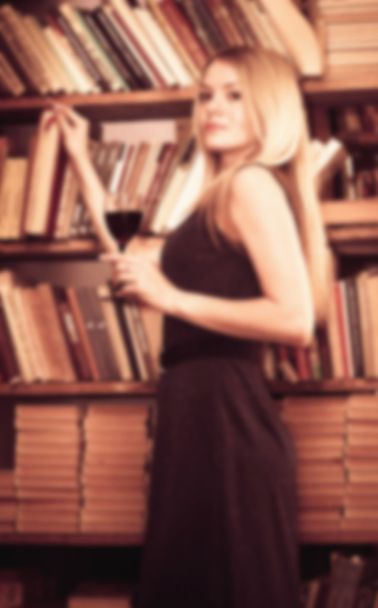 beautiful girl in an evening dress with a glass of wine in the luxurious interior of the library blurred toning - Фото, изображение