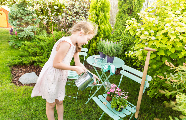 Child girl watering flowers outdoor in a summer garden - Photo, image