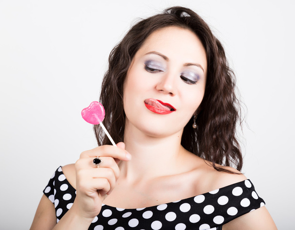 Portrait of happy beautiful young woman licking chupa chups. pretty woman with heart shaped lollipop - Foto, Imagem