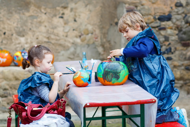 Kleine jongen en meisje schilderen met kleuren op pompoen - Foto, afbeelding