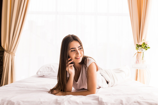 Νεαρό κορίτσι με το τηλέφωνο στο κρεβάτι της, στο σπίτι - Φωτογραφία, εικόνα