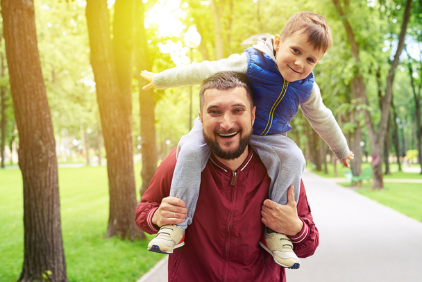  Батько їде зі своїм маленьким сином на плечах в парку в сонячний день
  - Фото, зображення