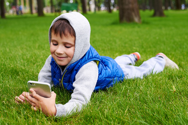  Malý chlapec ležící na zelené trávě s chytrýma telefonem  - Fotografie, Obrázek